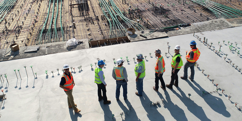 Construction men in high-vis vests and safety hats, lined up on a construction. Previewing the upcoming Joints Contracts Tribunal (JCT) 2024 suite of contracts site. 