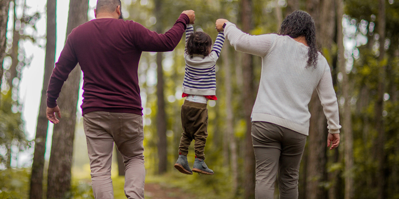 Man and Woman swinging child in the air playfully in an wooded area. The ‘one-stop shop’ for families—Family Hubs and Start for Life now open in local authorities across half the country