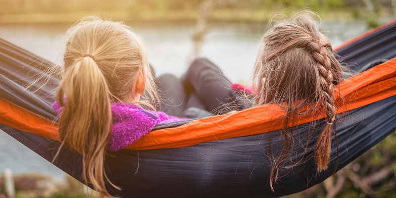 Two young girls sat on a hammock by a lakeside with their backs to the cameras. Seen but not heard: the child’s voice in the family court system