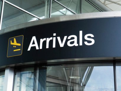 Russell-Cooke immigration law charging information. Image of airport arrivals signage above a glass door.