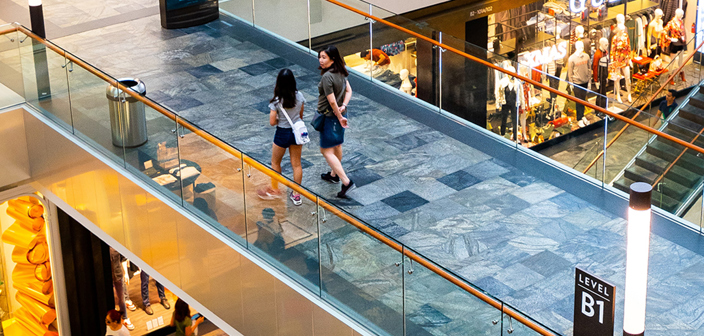 A shopping centre with two women walking over a tiled floor bridge above additional exposed floors and shops below