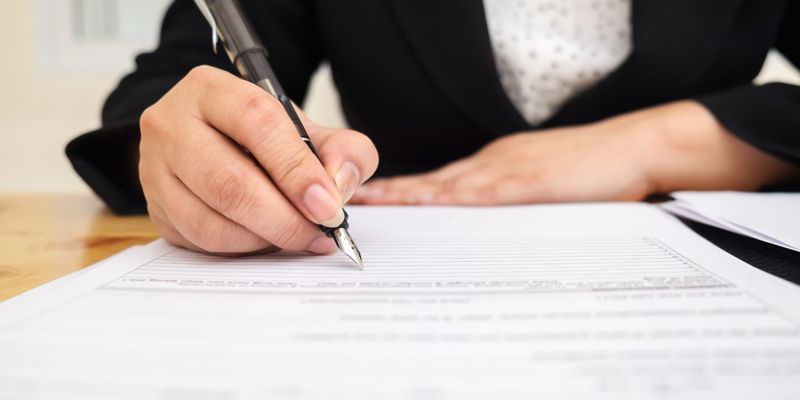 A business woman signing a document. Earn-outs explained: balancing risk and reward in M&A transactions