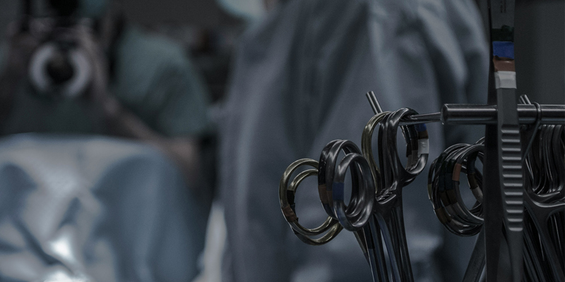 Surgical instruments in the foreground and surgeons operating in the background. Medical Practitioners Tribunal’s investigation into mesh surgeon, Mr Anthony Dixon
